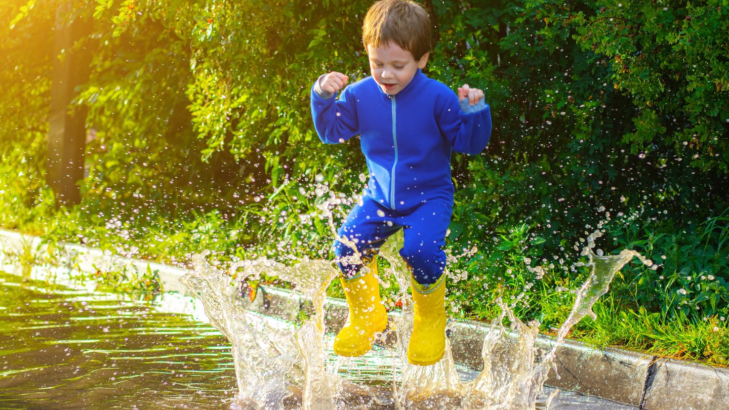 Ein Kind hüpft nach einem Regen in eine Pfütze (Foto: IMAGO, IMAGO / YAY Images)