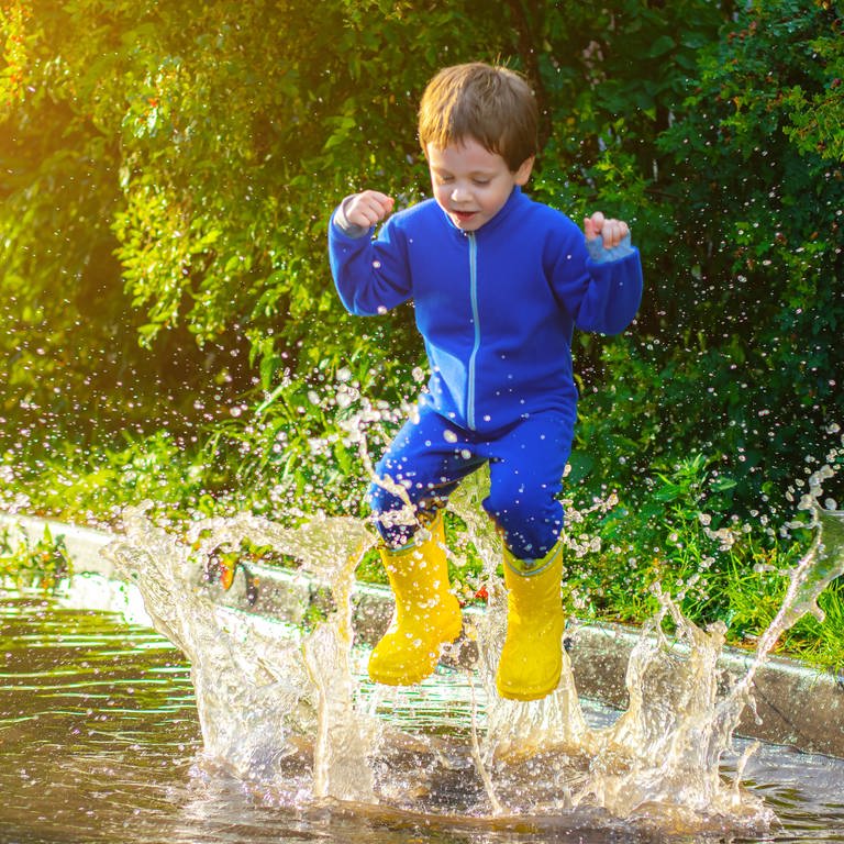 Ein Kind hüpft nach einem Regen in eine Pfütze (Foto: IMAGO, IMAGO / YAY Images)