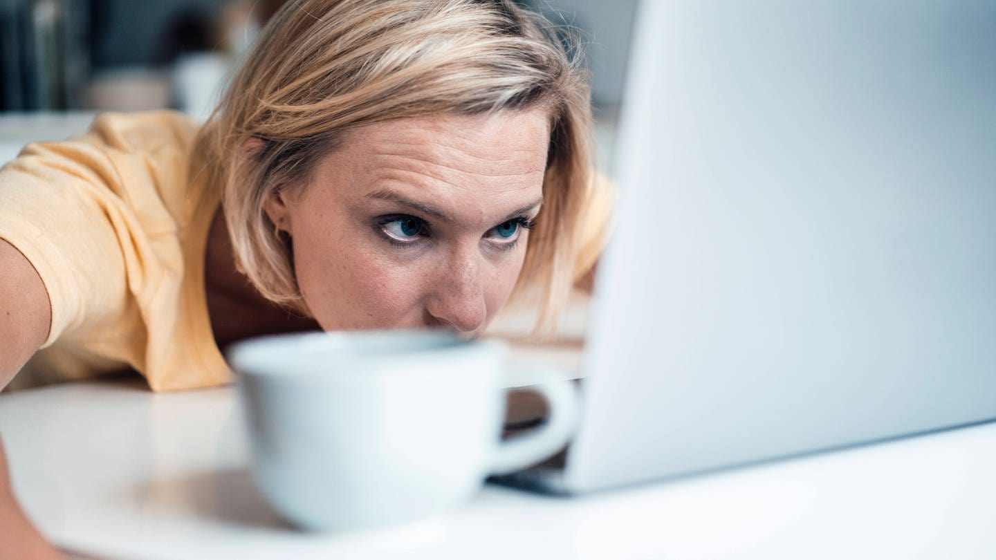 Frau liegt vor einem Laptop und schaut müde auf den Bildschirm: Wir brauchen mehr als ein Drittel unseres Gehirns, um unsere Augen zu bedienen. Wenn wir müde sind, ist unsere Sehrleistung deutlich geringer.
