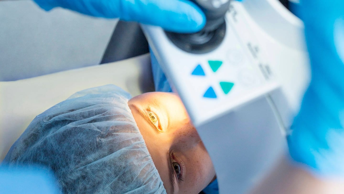 Operation am Auge einer Patienten mithilfe der Lasik-Methode. Die liegende Patientin trägt eine OP-Haube, ihr linkes Auge wird von einem medizinischen Gerät über ihr angeleuchtet. (Foto: IMAGO, IMAGO / Science Photo Library)