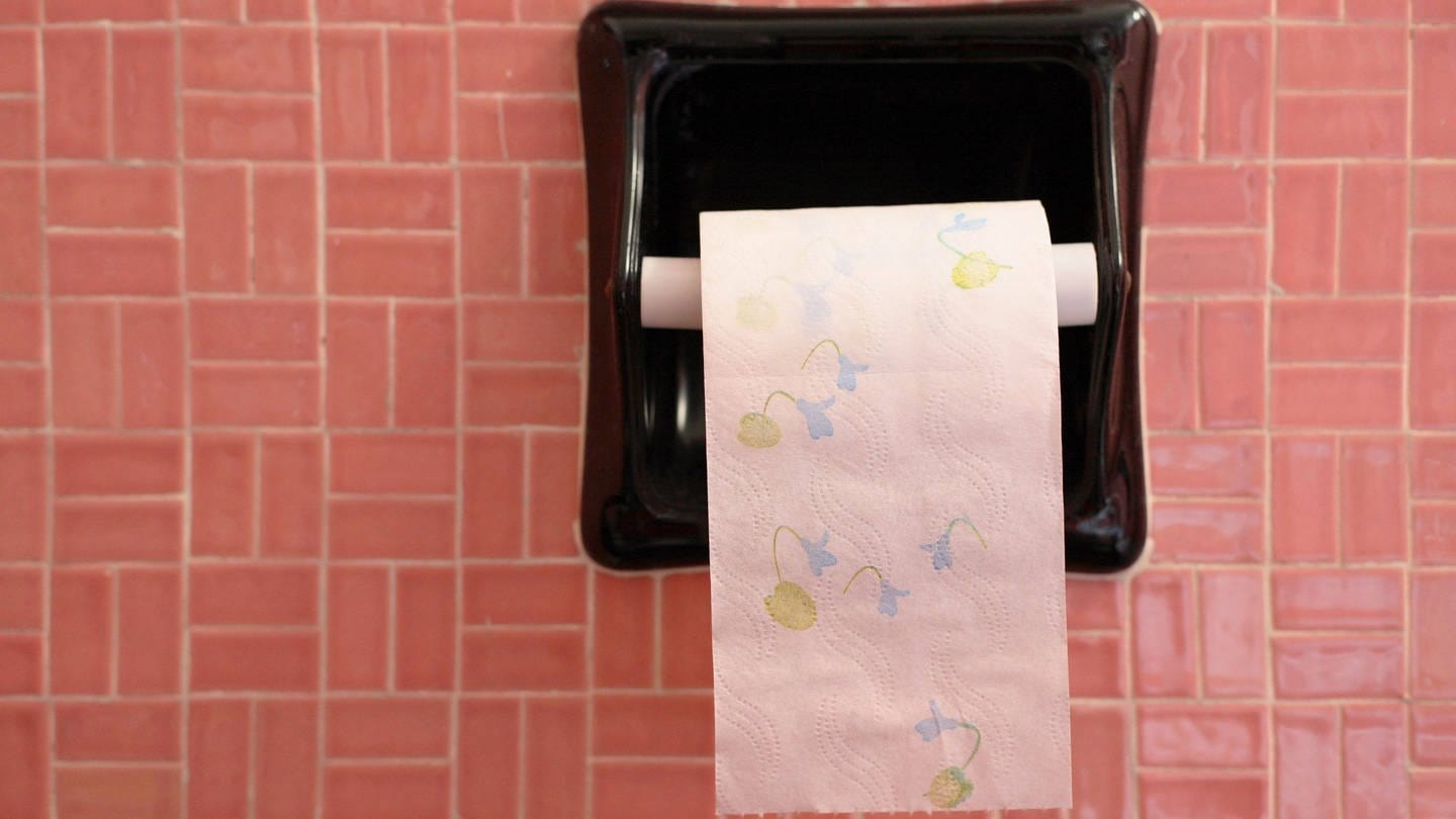 Geblümtes Klopapier hängt an einem Wandhalter vor rosa Kacheln: Am 26. August ist der Tag des Toilettenpapiers (Foto: IMAGO, IMAGO / blickwinkel)