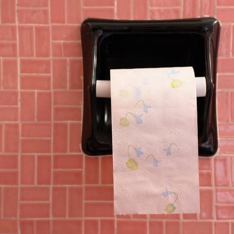 Geblümtes Klopapier hängt an einem Wandhalter vor rosa Kacheln: Am 26. August ist der Tag des Toilettenpapiers (Foto: IMAGO, IMAGO / blickwinkel)