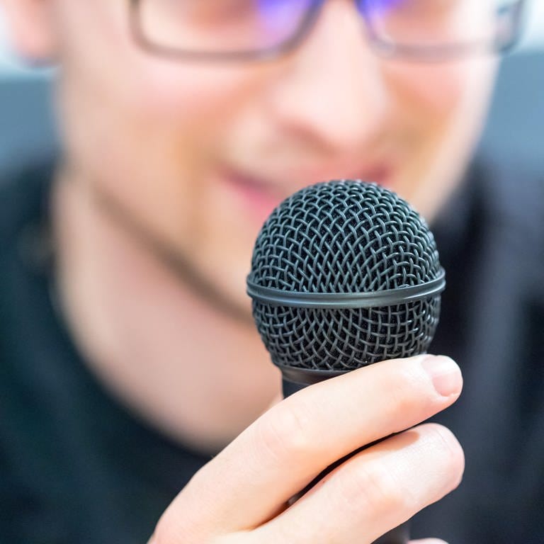Junger Mann hält Mikrofon vor dem Gesicht: Wenn man in ein Mikrofon spricht, kommt beim Mikrofon der Schall nur über die Luftleitung an – nicht über die Knochenleitung. Deshalb klingt es so anders. 