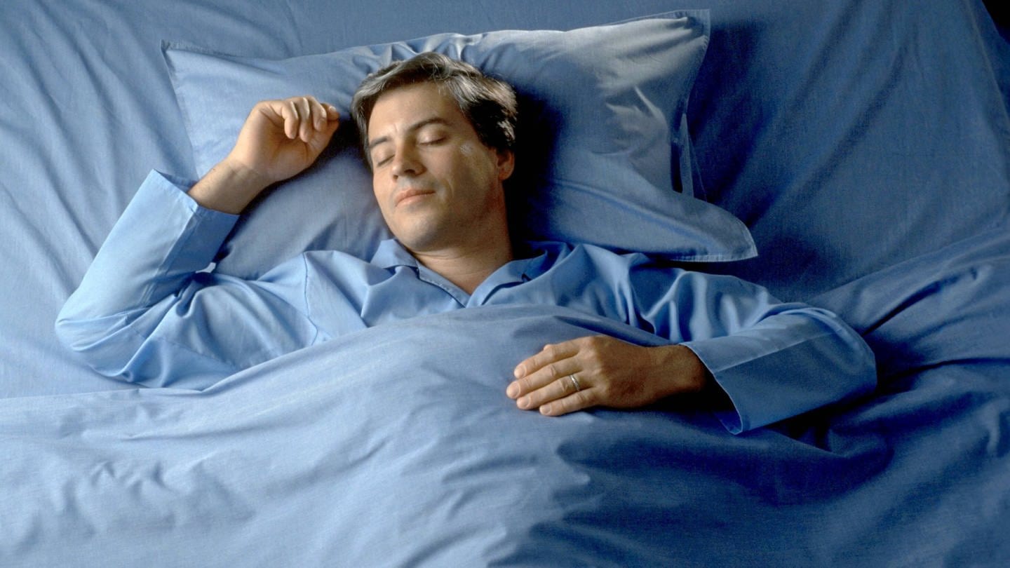 Ein Mann schläft auf dem Rücken im Bett: Ob träumen wichtig ist, das wissen wir gar nicht, weil jeder Mensch jede Nacht träumt – ob es wichtig ist oder nicht. (Foto: IMAGO, IMAGO / Paul von Stroheim)