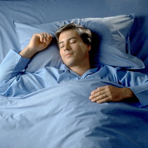 Ein Mann schläft auf dem Rücken im Bett: Ob träumen wichtig ist, das wissen wir gar nicht, weil jeder Mensch jede Nacht träumt – ob es wichtig ist oder nicht.  (Foto: IMAGO, IMAGO / Paul von Stroheim)