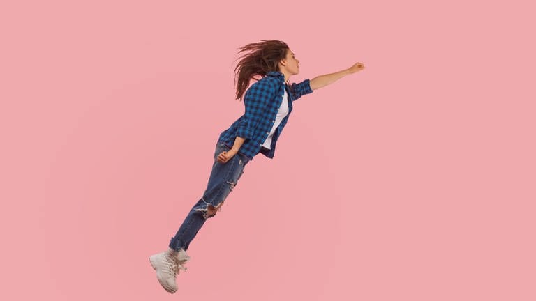 Junge Frau in Jeans und kariertem Hemd fliegt wie Superman durch die Luft: Die meisten Klarträume treten kurz vor dem Erwachen auf