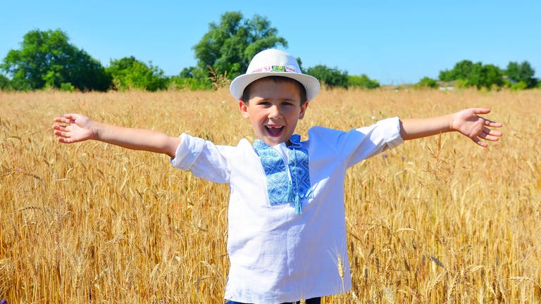Ein junge steht lachend mit ausgebreiteten Armen in einem Weizenfeld in der Ukraine: Die Ukraine wird auch "Kornkammer Europas" genannt. Das liegt vor allem an den Schwarzerde-Böden, die zu den besten Ackerböden der Welt gehören.