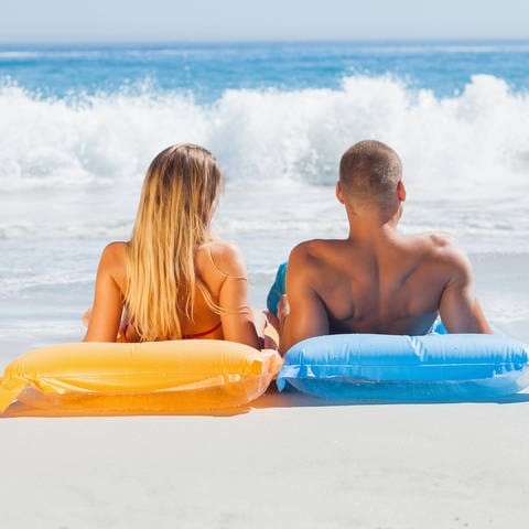 Eine Frau und ein Mann auf Luftmatratzen beim Sonnenbad am Strand: Bräune entsteht durch ein bestimmtes Farbpigment, das Melanin heißt. Es bildet sich unter der Haut, wenn UV-Strahlung auf die Hautzellen kommt. Diese UV-Strahlung, vor allem die UV-B-Strahlung, produziert das Melanin. (Foto: IMAGO, IMAGO / Panthermedia)