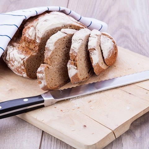 Holzbrett mit aufgeschnittenem Brot und Brotmesser: Zum Brotschneiden eignen sich Holzbretter. Zum Schneiden von Fleisch und Gemüse sollte man lieber Kunststoffbretter verwenden; sie lassen sich leichter reinigen und von Mikroorganismen befreien. (Foto: Colourbox)