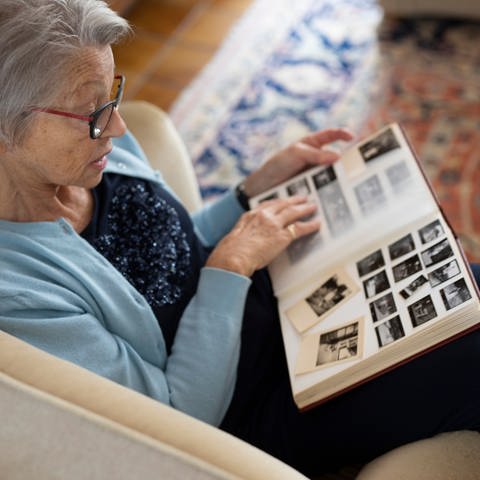 Grauhaarige Frau betrachtet Fotoalbum: Die Zuverlässigkeit der Erinnerung ist tatsächlich ungewiss. Wir erinnern die Dinge nicht immer nur, wie man etwa einen Film abspulen würde. Vielmehr erinnern wir die Dinge so, wie wir sie das letzte Mal erzählt haben, denn immer, wenn wir neu erzählen, wird wieder neu abgespeichert.  (Foto: picture-alliance / Reportdienste, picture alliance / photothek | Ute Grabowsky)