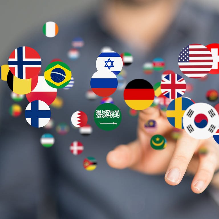 Runde Buttons mit Nationalflaggen schweben in der Luft und werden mit dem Finger angetippt: Insgesamt gibt es auf der Welt ungefähr 7.000 Sprachen. Die Sprachenvielfalt konzentriert sich insbesondere um den Äquator herum. (Foto: IMAGO, IMAGO / Wirestock)