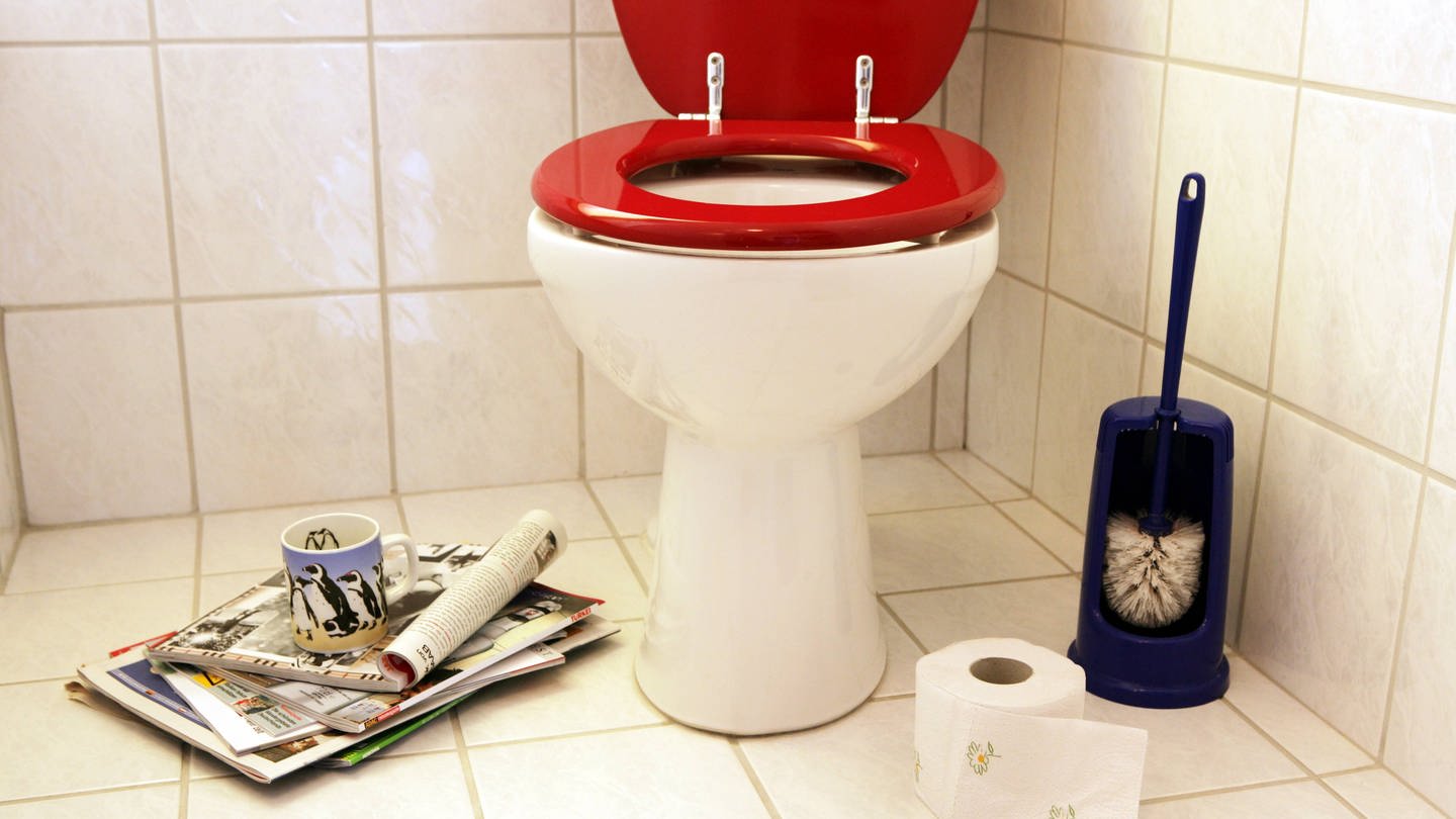 Zeitschriften und eine Kaffeetasse sorgen für Kurzweil und Entspannung auf der Toilette mit roter Klobrille: Der Ekel vor Fäkalien ist allerdings ein angeborenes Gefühl und dient als Schutzmechanismus. (Foto: IMAGO, IMAGO / Jochen Tack)