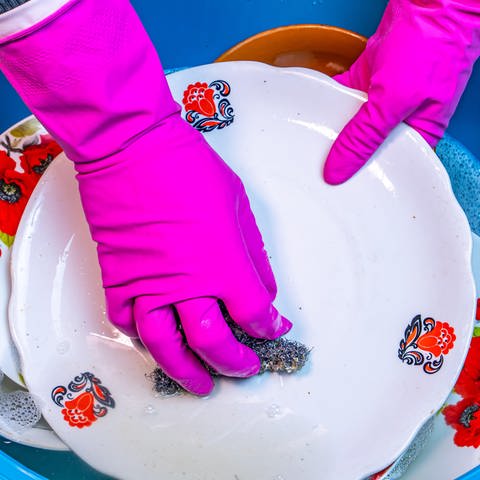 Hände in pinkfarbenen Handschuhen spülen einen Teller: Beim Spülen sollte man darauf achten, die Lappen regelmäßig zu wechseln. Spültücher mit eingewebten Silverfäden bringen keinen zusätzlichen Nutzen in Bezug auf die Hygiene. (Foto: picture-alliance / Reportdienste, picture alliance / PantherMedia | -)