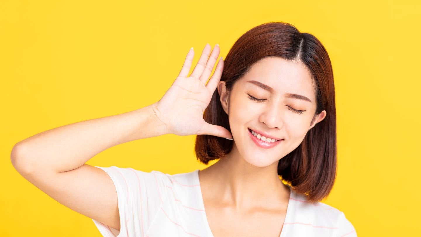 Junge Frau hält sich lauschend eine Hand hinter das Ohr: Absolutes Gehör bedeutet, dass ich zu jemandem sagen kann 