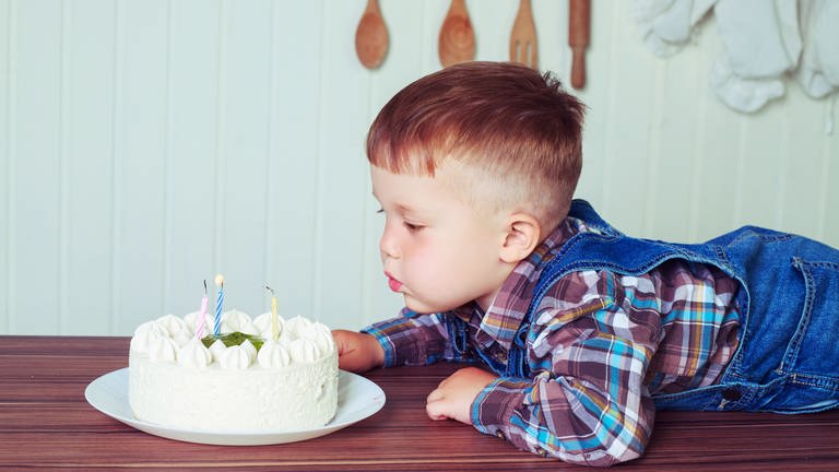 Ein Junge pustet Kerzen auf einer Geburtstagstorte aus
