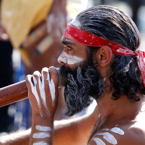 Aborigine bläst in ein Didgeridoo: Seit 1925 kennt man das Blasinstrument der australischen Aborigines in England als Didgeridoo. Die Ursprünge des Instruments liegen allerdings viel länger zurück: 2000 Jahre sagen die Forscher – 40.000 Jahre sagen die Aborigines