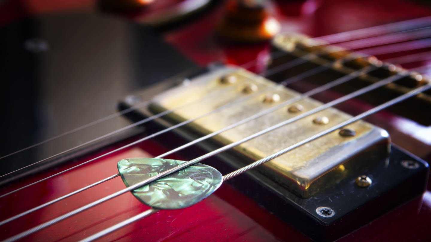 Akustikgitarre mit Plektrum: Das Plektrum oder Plektron verwendet man zum Anschlagen von Saiten. Es wird aus Kunststoff hergestellt, heute Nylon. (Foto: IMAGO, IMAGO / agefotostock)
