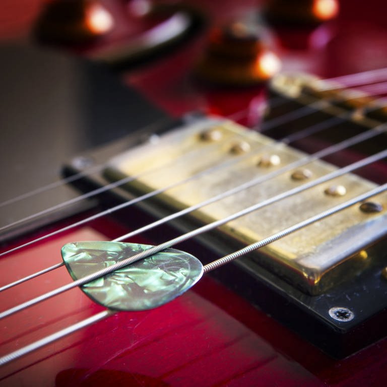 Akustikgitarre mit Plektrum: Das Plektrum oder Plektron verwendet man zum Anschlagen von Saiten. Es wird aus Kunststoff hergestellt, heute Nylon.