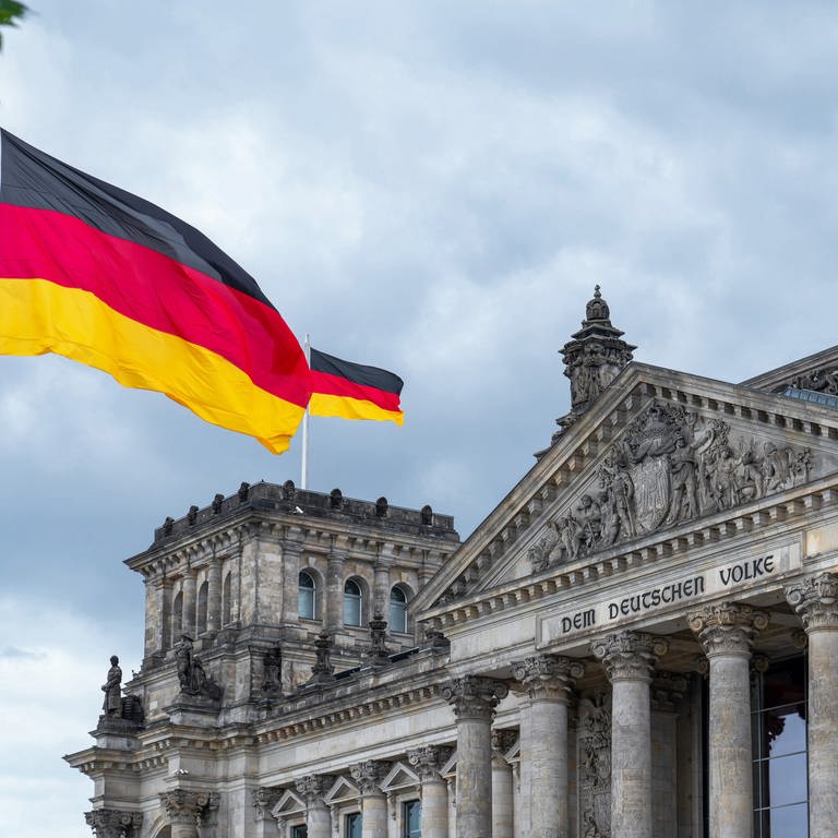 Bundesflagge der Bundesrepublik Deutschland mit den Farben schwarz, rot, gold weht vor und auf dem Reichstagsgebäude in Berlin