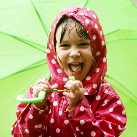 Lachendes Kind im roten Regenmantel mit grünem Schirm: Seriöse Wettervorhersagen sind maximal für 5 is 7 Tage möglich. Eine gewisse Toleranz muss immer einkalkultiert werden