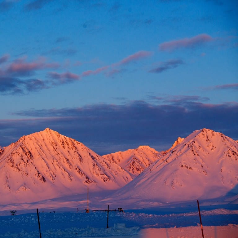 Von der untergehenden Sonne rot angeleuchtet sind die schneebedeckte bis zu 1.000 Meter hohe Berge am 9 April 2015 in der Nähe der Forschungsstation Kings Bay in Ny-Ålesund auf Spitzbergen (Norwegen) zu sehen. Ab dem Polarkreis geht die Sonne an manchen Sommertagen gar nicht mehr unter.