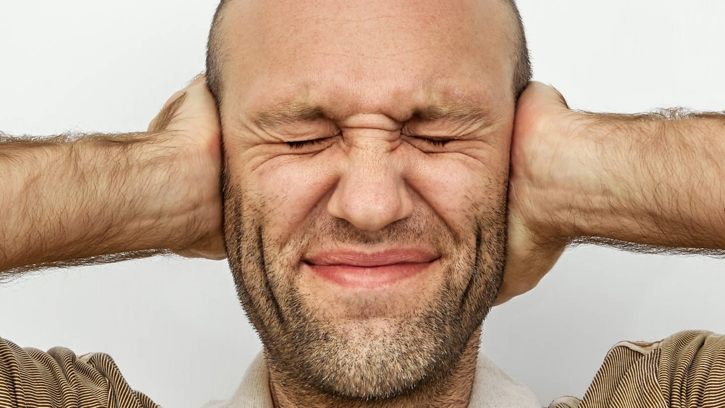 Ein Mann hält sich mit geschlossenen Augen gestresst die Ohren zu: Stresserfahrungen werden in der Großhirnrinde als Gedächtnisspuren abgelegt (Foto: Colourbox)