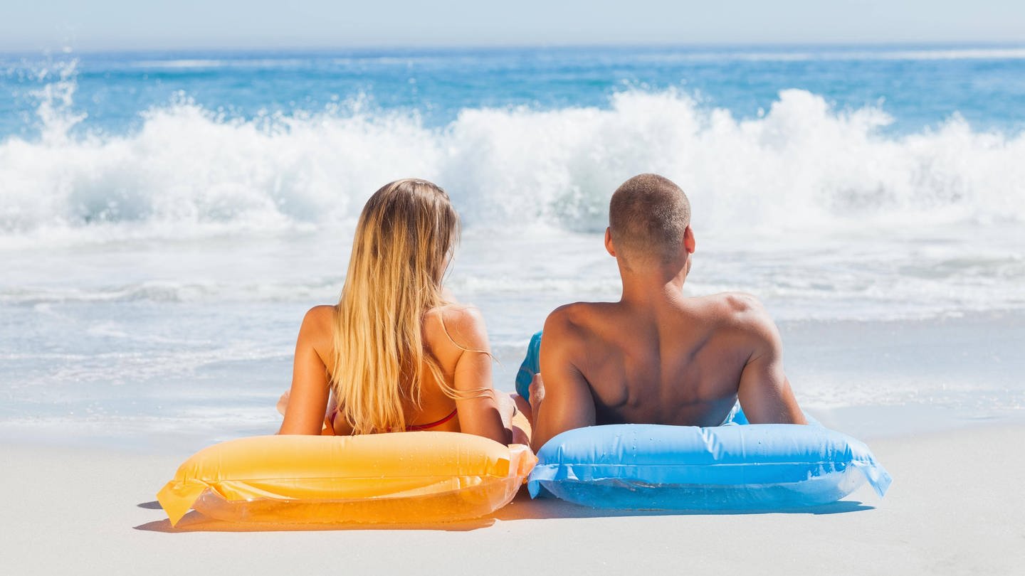 Eine Frau und ein Mann auf Luftmatratzen beim Sonnenbad am Strand: Bräune entsteht durch ein bestimmtes Farbpigment, das Melanin heißt. Es bildet sich unter der Haut, wenn UV-Strahlung auf die Hautzellen kommt. Diese UV-Strahlung, vor allem die UV-B-Strahlung, produziert das Melanin.