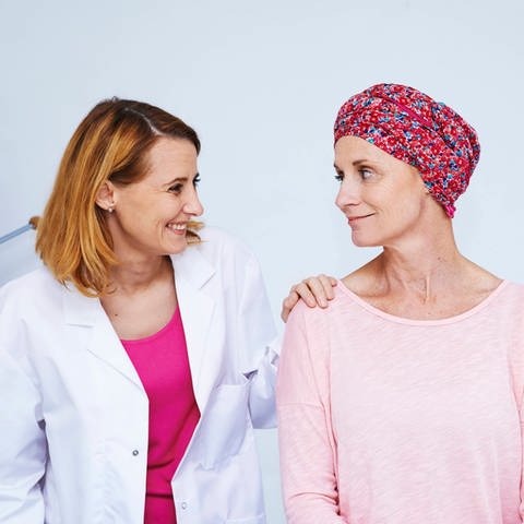Krebspatientin im Gespräch mit einer Ärztin, die ihr die Hand auf die Schulter legt: An vielen Zentren, die sich mit der Behandlung von Krebserkrankunen beschäftigen, auch psychoonkologischer Beistand gegeben. Denn wenn man sich seelisch besser mit der Krankheit auseinandersetzen kann, kann man den Krebs insgesamt besser bekämpfen.
