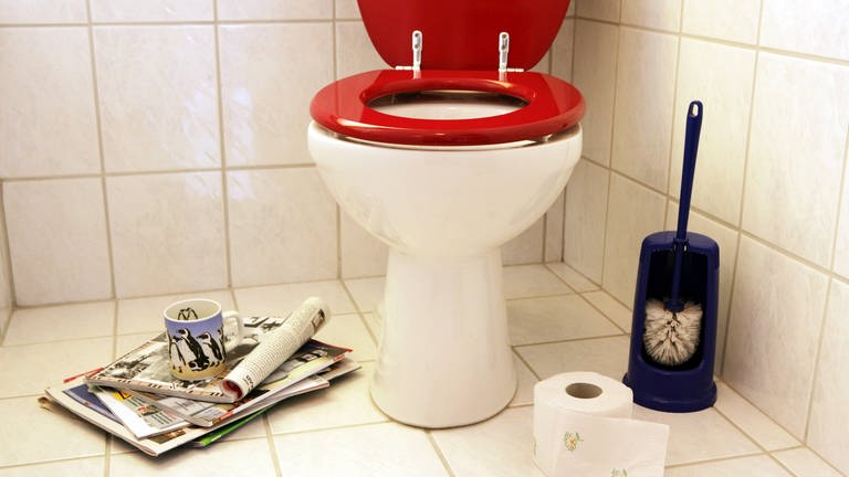 Zeitschriften und eine Kaffeetasse sorgen für Kurzweil und Entspannung auf der Toilette mit roter Klobrille: Der Ekel vor Fäkalien ist allerdings ein angeborenes Gefühl und dient als Schutzmechanismus.