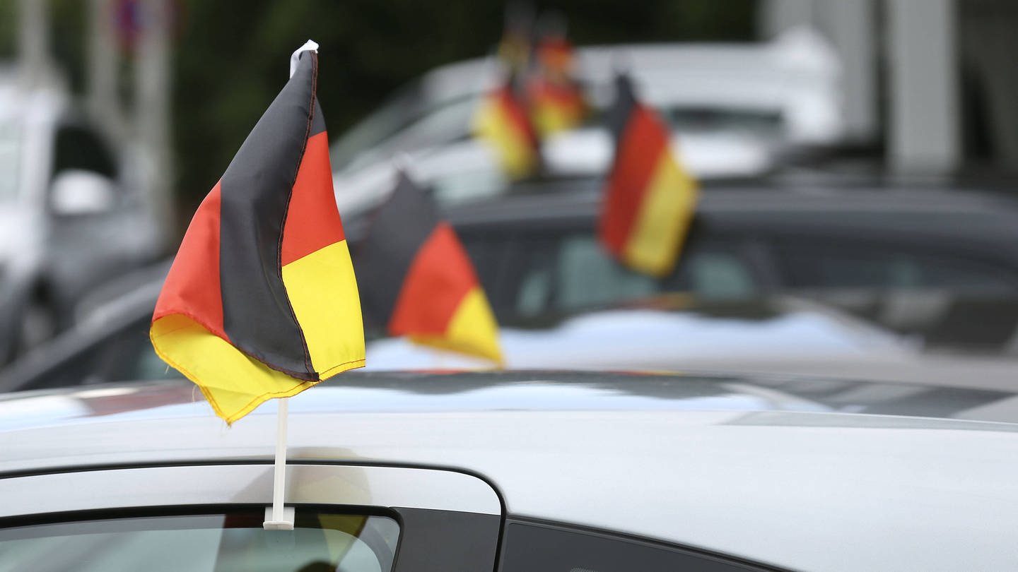 Deutschlandfähnchen an einem Auto:  Wenn jedes Auto mit zwei Fähnchen im Schnitt während eines Fußballturniers 100 Kilometer zurücklegt, bedeutet dies bundesweit einen Mehrverbrauch von rund 3 Millionen Litern. (Foto: IMAGO, IMAGO / Claus Bergmann)