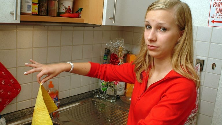 Eine junge Frau hält mit spitzen Fingern ein Spültuch: Wer ist in der Küche ist die größere Keimschleuder: Lappen oder Schwamm? Wir erklären die richtige Waschtemperatur und das geeignete Waschmittel.
