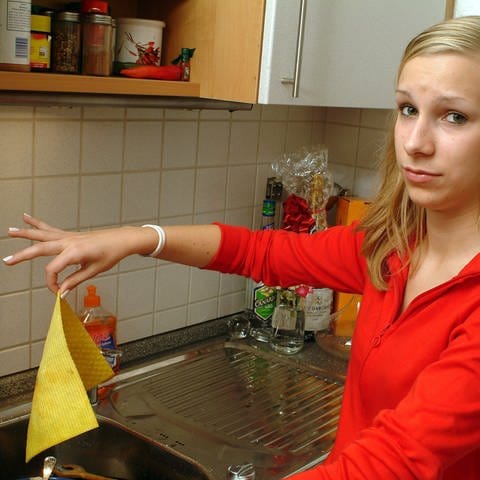 Eine junge Frau hält mit spitzen Fingern ein Spültuch: Wer ist in der Küche ist die größere Keimschleuder: Lappen oder Schwamm? Wir erklären die richtige Waschtemperatur und das geeignete Waschmittel. (Foto: picture-alliance / Reportdienste, picture-alliance / dpa | Heiko Wolfraum)