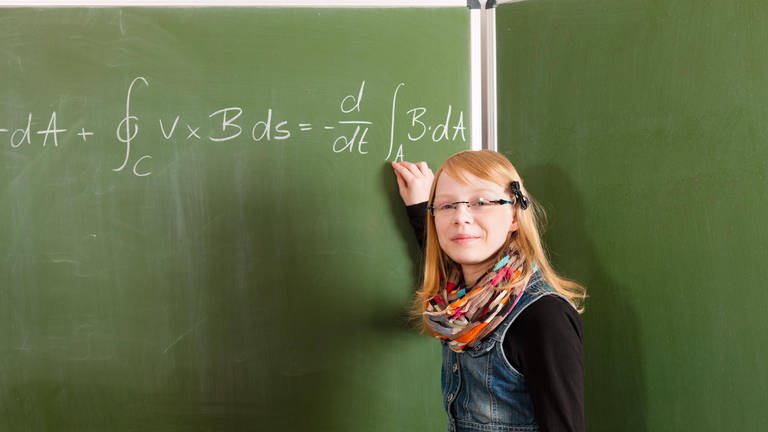 Schülerin steht vor Tafel mit Formel (Foto: IMAGO, imago images / Panthermedia)