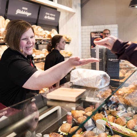 Bäckereifachverkäuferin nimmt in einer Bäckerei Bargeld entgegen