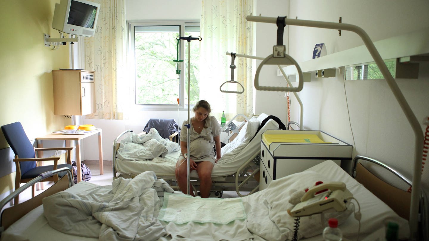 Schwangere mit Schmerzen sitzt allein auf einem Krankenhausbett