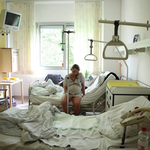Schwangere mit Schmerzen sitzt allein auf einem Krankenhausbett (Foto: IMAGO, imago stock&people)