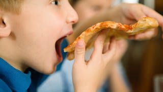 Ein junge isst Pizza (Foto: imago images, MarkxHunt)