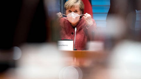Angela Merkel nimmt ihre Maske ab. (Foto: IMAGO, imago images/IPON)