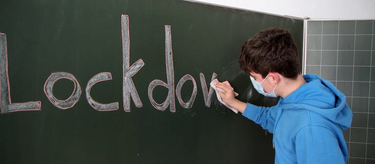 Schüler wischt "Lockdown"-Aufschrift von Tafel (Foto: IMAGO, IMAGO / Eibner)