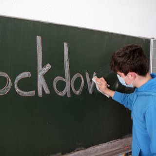 Schüler wischt "Lockdown"-Aufschrift von Tafel (Foto: imago images, IMAGO / Eibner)