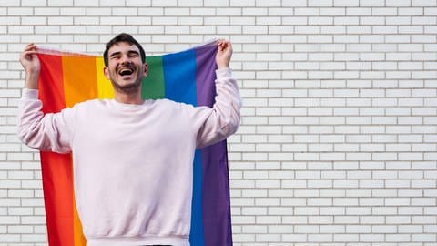 Junger Mann mit Regenbogenflagge: Jugendliche interessieren sich heute sehr für sexuelle Vielfalt und Identität (Foto: IMAGO, IMAGO / Cavan Images)