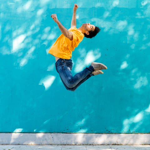 Mann springt vor blauer Wand hoch in die Luft. Was ist Schwerkraft? (Foto: imago images, IMAGO / Westend61)