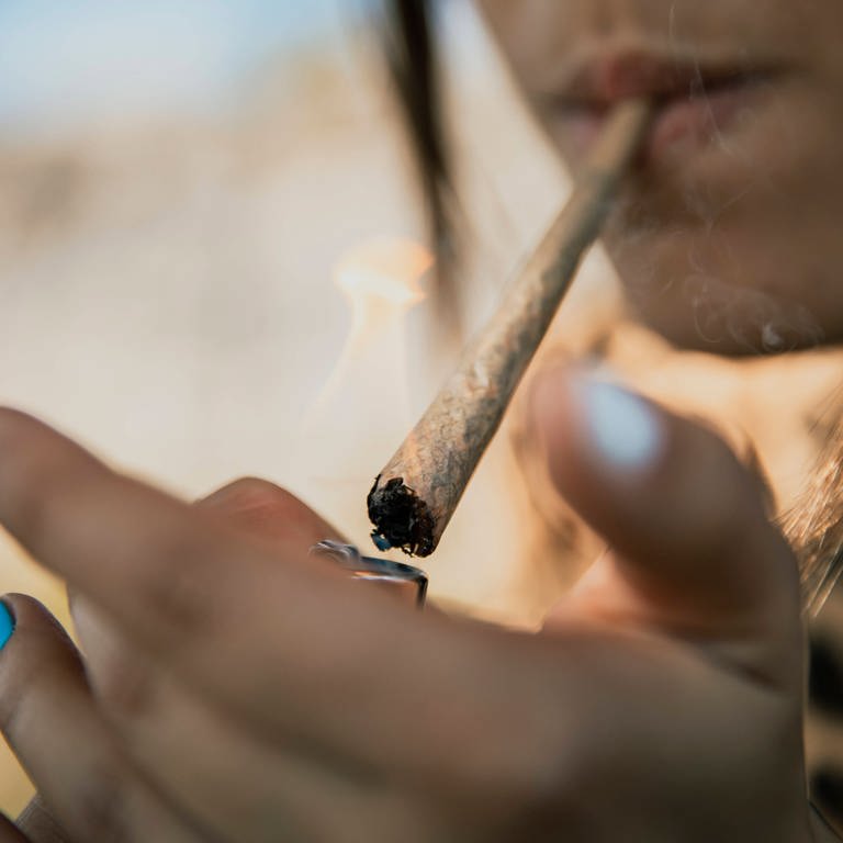 Junge Frau zündet sich eine Zigarette mit Marihuana an. (Foto: IMAGO, MAGO / Westend61)