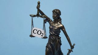 Justitia-Figur hebt eine Waage vor sich, auf der ein Schild mit Aufschrift "CO2" steht. (Foto: imago images, IMAGO / Steinach)