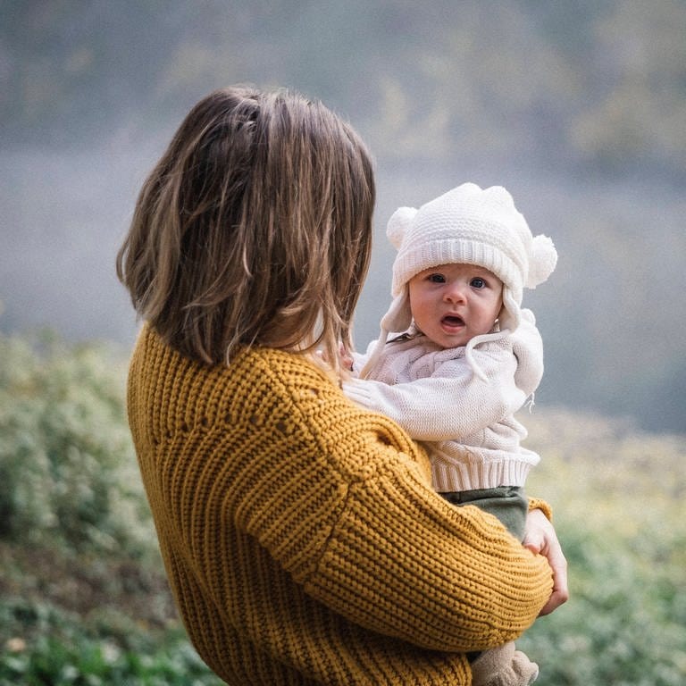 Baby auf dem Arm seiner Mutter vor einem See im Hintergrund (Foto: IMAGO, Evgeny Vasenev via www.imago-images.de)