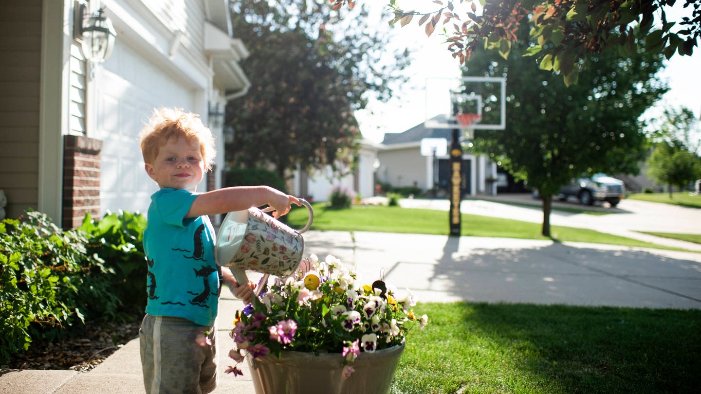 Ein Junge gießt Blumen in der Sonne (Foto: IMAGO, imago images/Cavan Images)