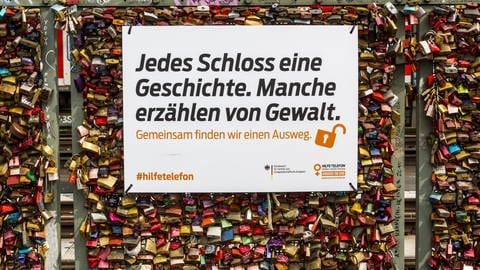 Liebesschlösser auf der Hohenzollern Brücke in Köln mit Infotafel des Bundesamt für Familie und zivilgesellschaftliche Aufgaben gegen Gewalt in der Beziehung