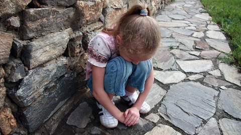 Mädchen hockt vor einer Mauer. Wenn Kinder aufgrund von Rheuma ständig heftige Schmerzen haben, beginnen sie, schmerzauslösende Bewegungen zu vermeiden (Foto: IMAGO, altanaka)