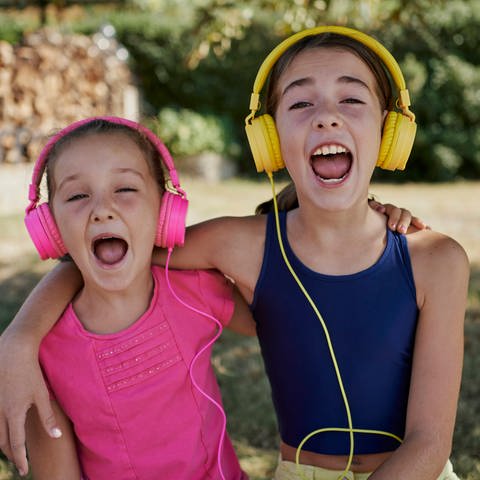 Zwei Mädchen mit Kopfhörern singen mit weit geöffneten Mündern (Foto: IMAGO, Cavan Images via www.imago-images.de)