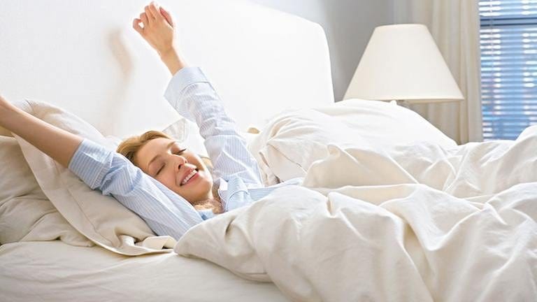 Frau liegt im Bett und streckt sich nach dem Wachwerden. (Foto: Getty Images, Thinkstock -)